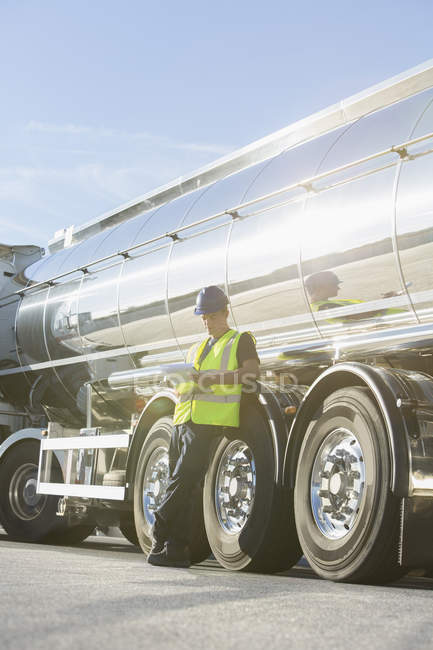 Worker with clipboard leaning on stainless steel milk tanker — Stock Photo