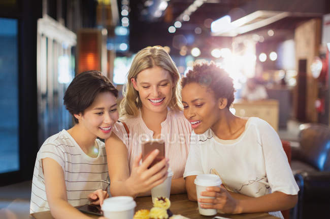 Young women friends using cell phone and drinking coffee in cafe — Stock Photo
