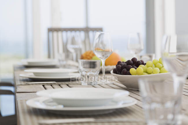Früchte auf Tellern über dem Tisch mit leeren Gläsern — Stockfoto