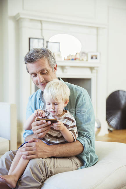 Padre e hijo usando el teléfono celular en la sala de estar - foto de stock
