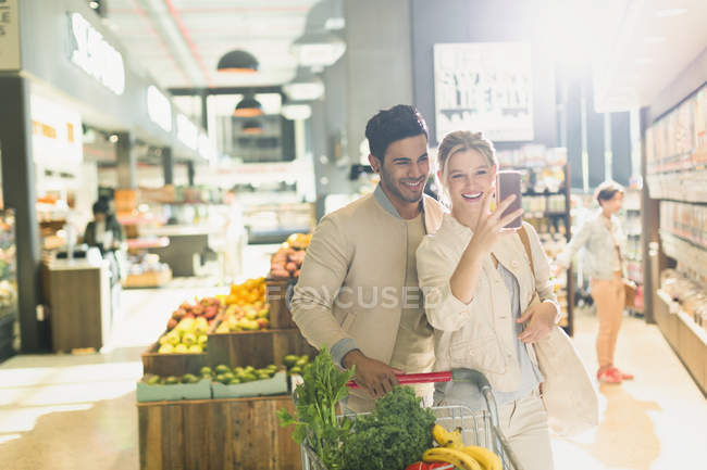 Sourire jeune couple prendre selfie dans le marché de l'épicerie — Photo de stock