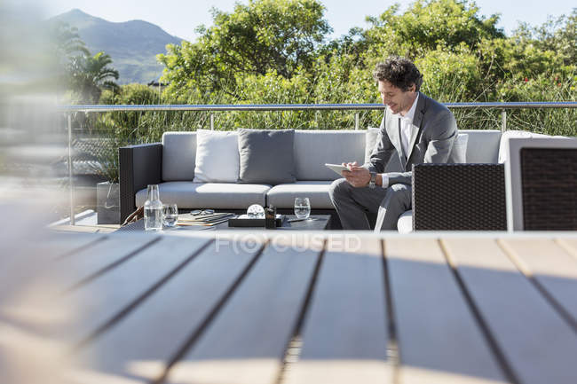 Empresário usando tablet digital na varanda de luxo ensolarado sofá pátio — Fotografia de Stock
