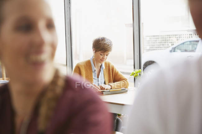 Femme avec écouteurs utilisant une tablette numérique à la fenêtre du café — Photo de stock