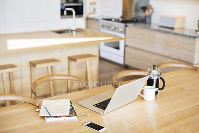 Laptop, French press coffee, cell phone and notebook on kitchen table — Stock Photo