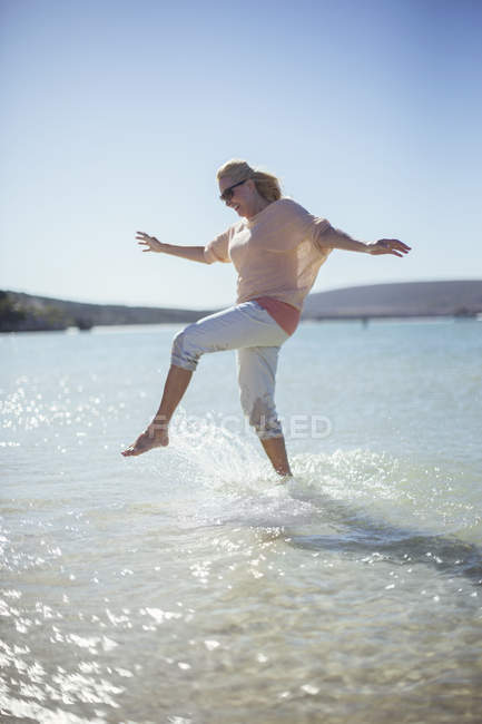Mulher espirrando na água na praia — Fotografia de Stock