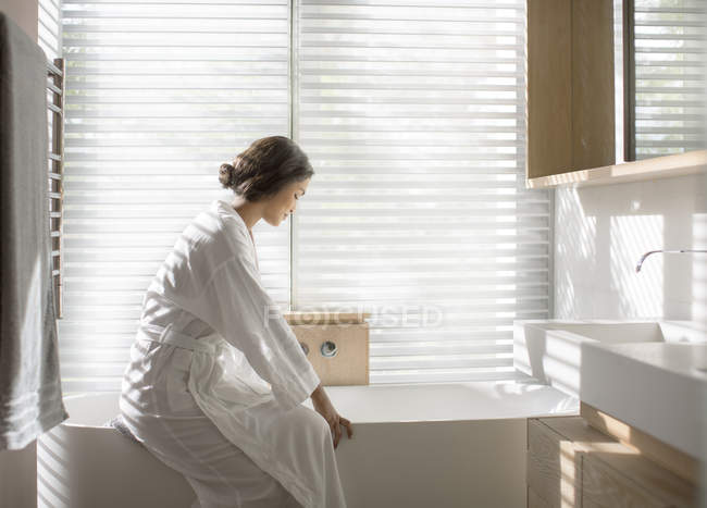Женщина в халате делает ванну в мокрой ванне в роскошной ванной — стоковое фото