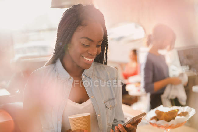 Smiling woman using cell phone and drinking coffee in cafe — Stock Photo
