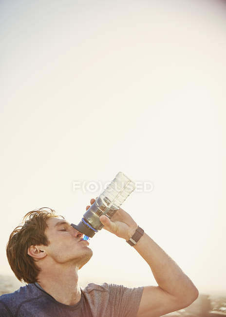 Thirsty male runner drinking water from water bottle — Stock Photo