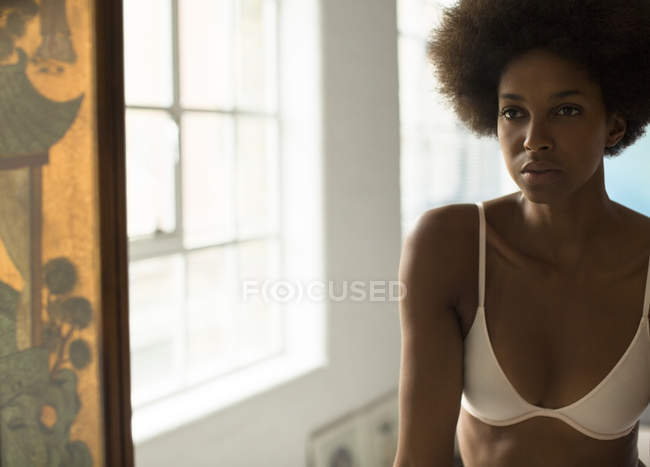 Serious woman in bra standing at mirror at home — Stock Photo