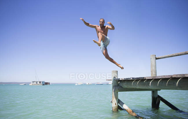 Couple jumping off wooden dock into water — Stock Photo