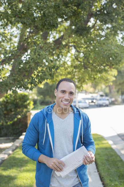 Portrait of smiling man with newspaper on sidewalk — Stock Photo