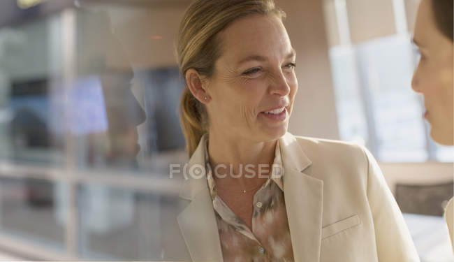 Улыбающаяся деловая женщина разговаривает с коллегой в офисе — стоковое фото