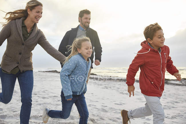 Familia juguetona corriendo en la playa de invierno - foto de stock