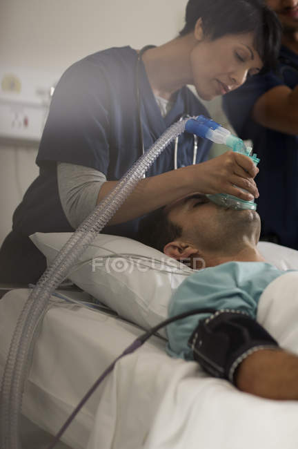 Médico sosteniendo máscara de oxígeno sobre la boca del paciente masculino en la unidad de cuidados intensivos - foto de stock