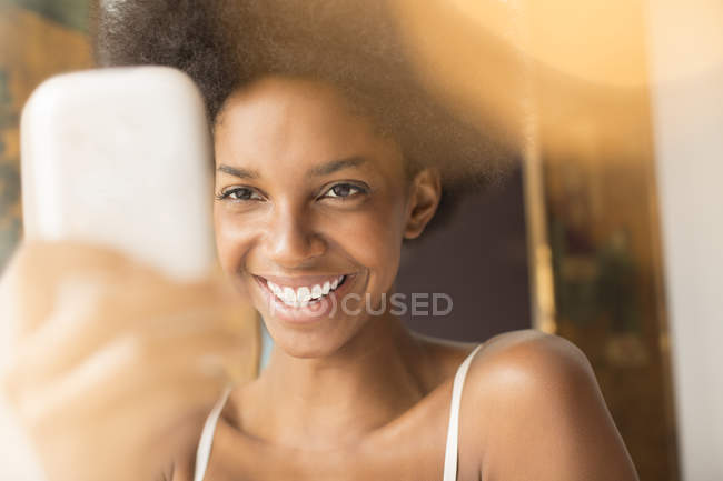 Mulher sorridente usando telefone celular em casa — Fotografia de Stock
