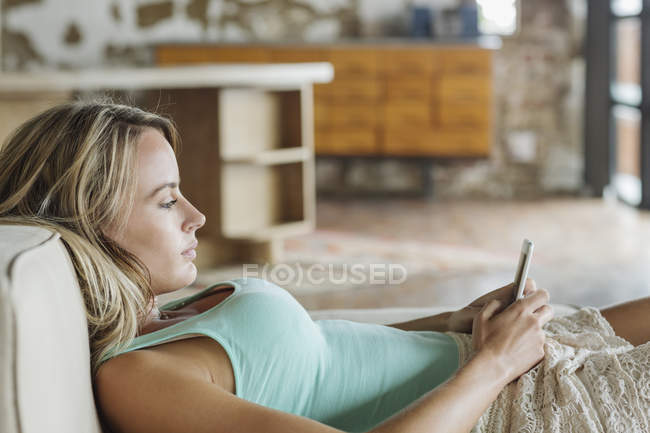 Mulher deitada no sofá e mensagens de texto com telefone celular — Fotografia de Stock