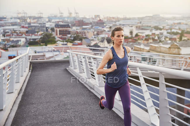 Female runner running on urban footbridge — Stock Photo