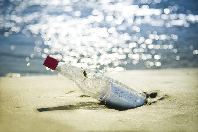 Mensaje en botella en playa contra agua - foto de stock