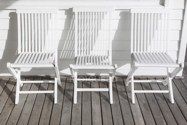 Sedie pieghevoli bianche in fila sul patio soleggiato — Foto stock