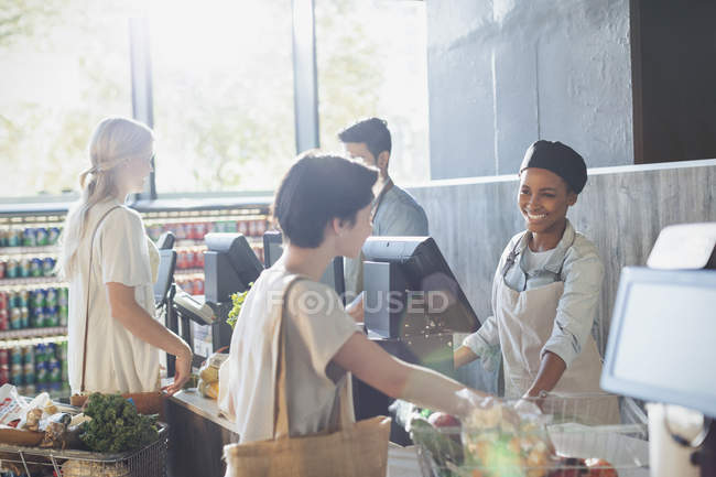 Smiling female cashier helping customer at grocery store checkout — Stock Photo