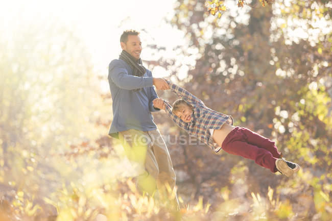 Padre girando hijo entre las hojas de otoño - foto de stock