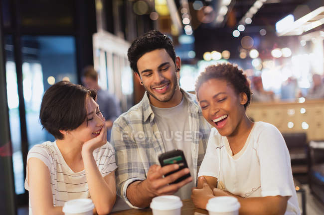 Giovani amici che usano il cellulare, messaggiano e ridono al caffè — Foto stock