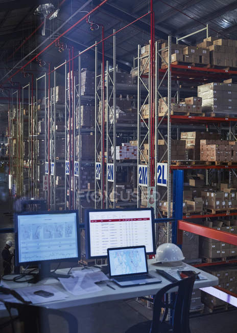 Bureau avec ordinateur portable et ordinateurs dans l'entrepôt de distribution — Photo de stock