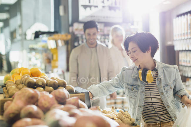 Mujer joven con auriculares compras de comestibles, productos de navegación en el mercado - foto de stock