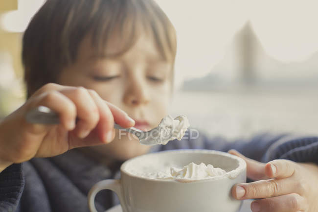 Close up boy scooping and eating whipped cream off hot cocoa — Stock Photo