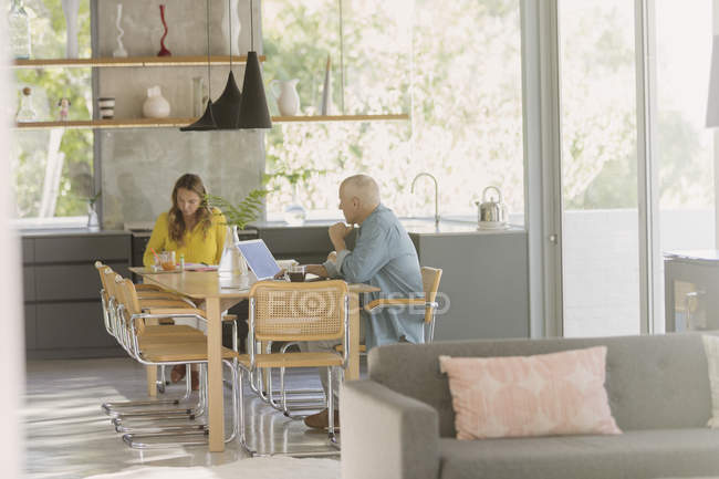 Зрелая пара работает за ноутбуком и ест за обеденным столом — стоковое фото