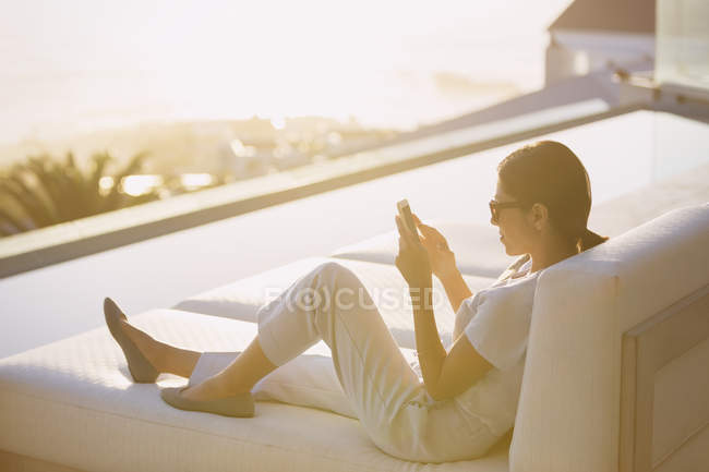Mulher usando telefone celular no salão de chaise na beira da piscina no pátio de luxo — Fotografia de Stock