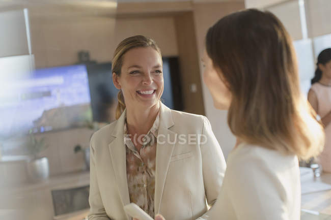 Улыбающиеся деловые женщины разговаривают в офисе — стоковое фото
