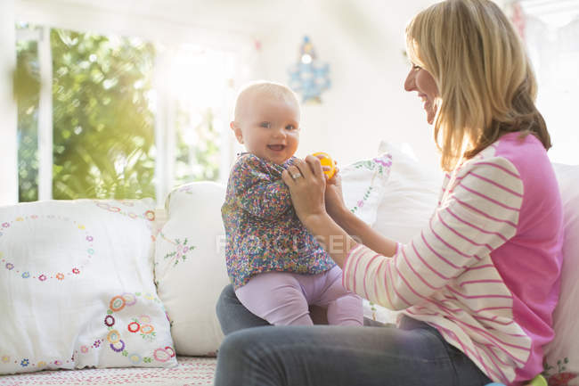 Mother playing with baby girl on sofa — Stock Photo