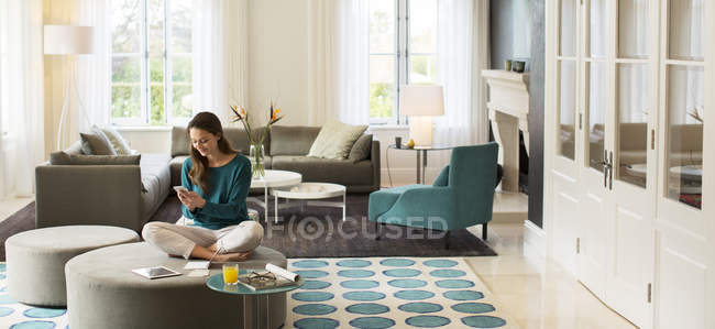 Женщина пишет смс на мобильный телефон на диване в гостиной — стоковое фото