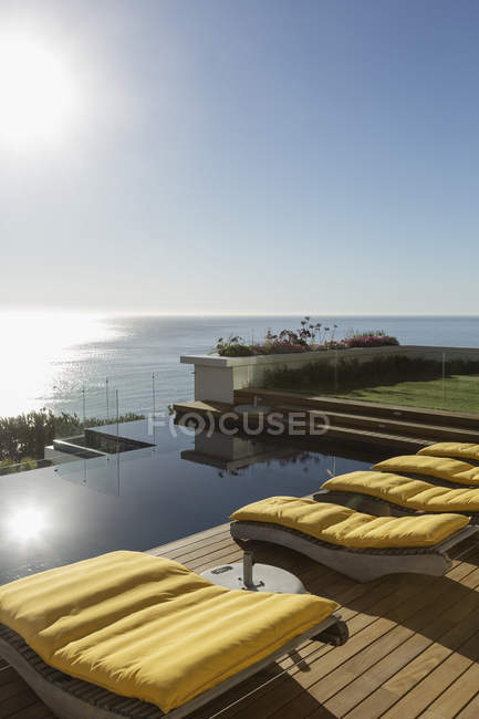 Soleil brille sur les chaises longues au bord de la piscine surplombant l'océan — Photo de stock