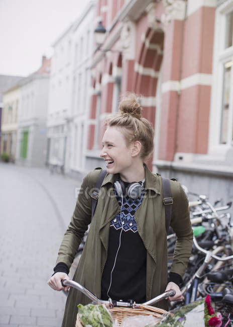 Усміхнена молода жінка з навушниками їде на велосипеді на міській вулиці — стокове фото