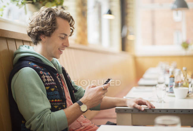 Glücklicher junger Mann benutzt Handy in Café — Stockfoto