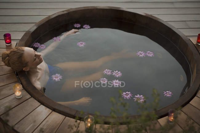 Femme sereine trempant dans un bain à remous avec des fleurs et des bougies sur le patio — Photo de stock
