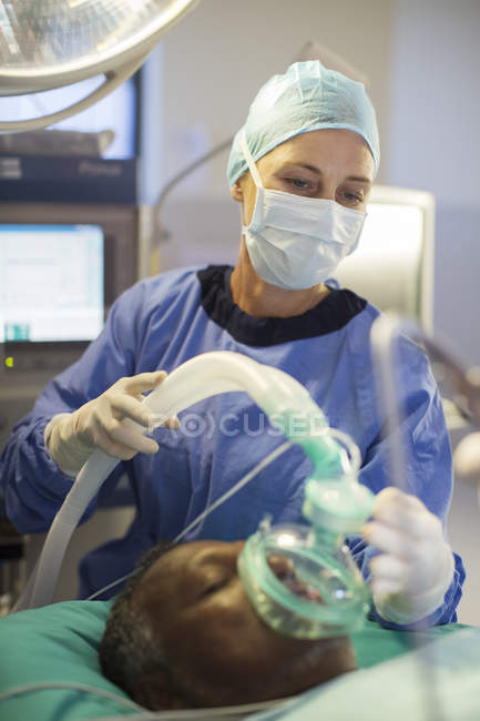 Anestesiólogo con máscara de oxígeno sobre la cara del paciente en quirófano - foto de stock