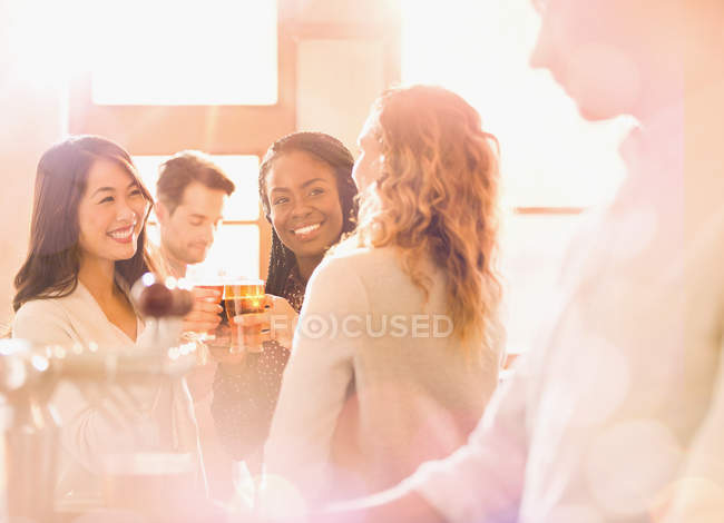 Freundinnen stoßen in sonniger Bar auf Biergläser an — Stockfoto