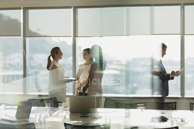 Mulheres de negócios conversando, usando laptop em reunião sala de conferências ensolarada — Fotografia de Stock
