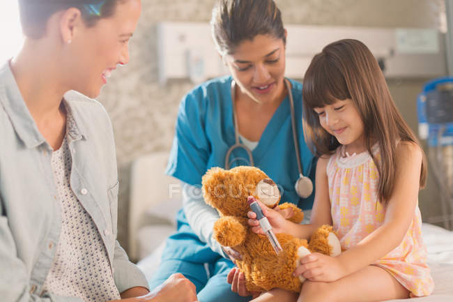 Female nurse and mother watching girl patient using insulin pen on teddy bear — Stock Photo