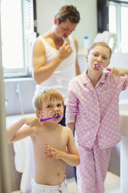 Padre e hijos cepillándose los dientes en el baño - foto de stock
