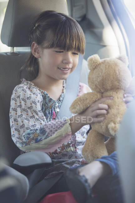 Menina com ursinho de pelúcia no banco de trás do carro — Fotografia de Stock