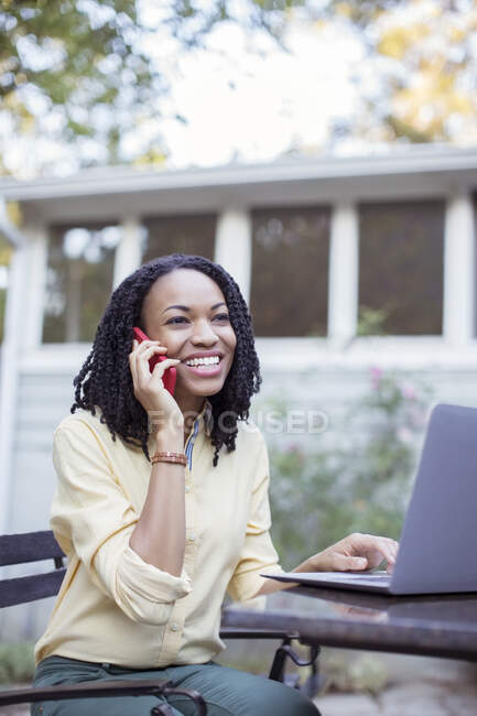 Щаслива жінка розмовляє на мобільному телефоні в ноутбуці на патіо — стокове фото