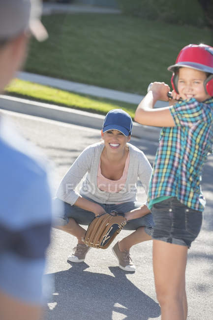 Family playing baseball in street — Stock Photo