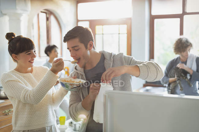 Jovem mulher alimentando namorado cereal na cozinha do apartamento — Fotografia de Stock
