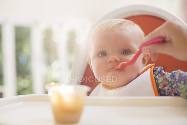Femme main nourrissant bébé fille en chaise haute — Photo de stock