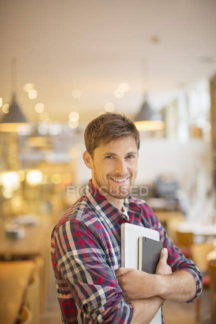 Happy young man holding books in cafe — Stock Photo