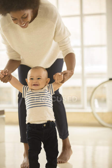 Madre ayudando a bebé niño caminar en el suelo en casa - foto de stock
